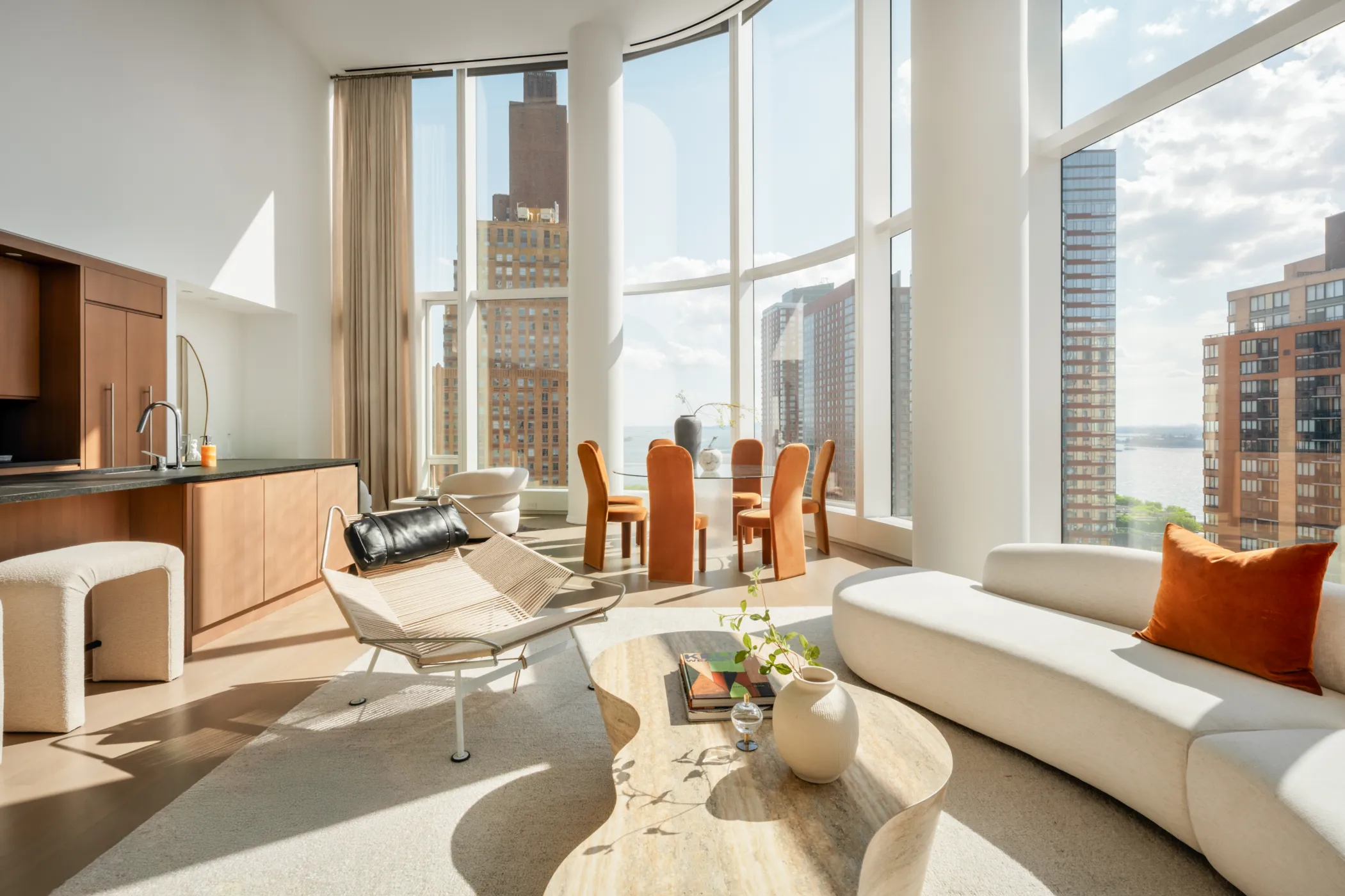 50 West NYC Condo Model Apartment Interior of living room, dining room and kitchen with double-height wall of windows overlooking NYC skyline and river